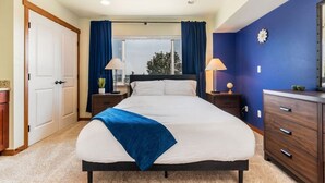 A bedroom with a bed, two bedside tables, a dresser, and a window with curtains.