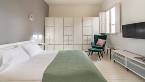 Ein Schlafzimmer mit einem Bett, einem grünen Sessel, einem Fernseher und einem Kleiderschrank.