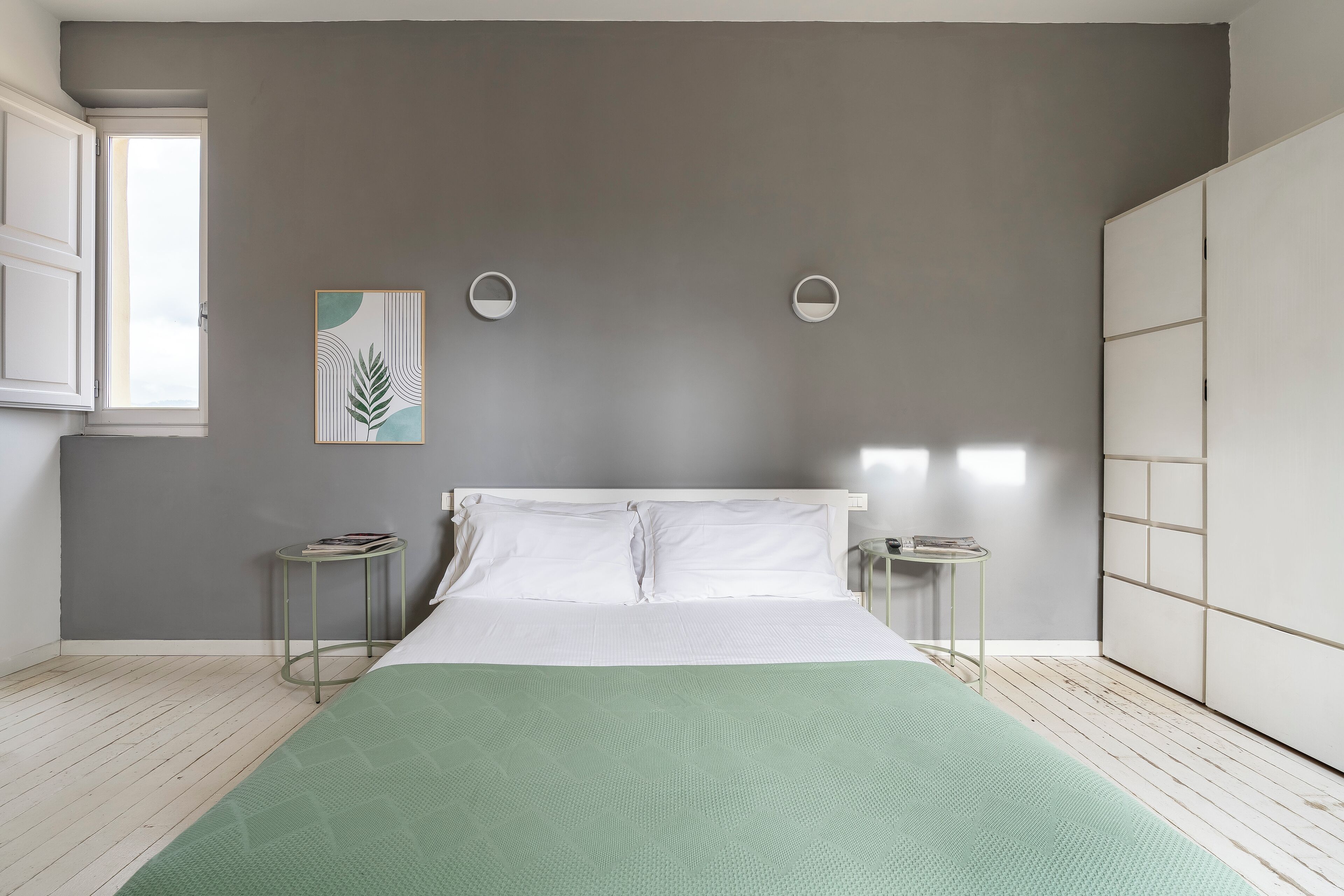 A bedroom with a bed, a bedside table, a nightstand, a wardrobe, and a window.