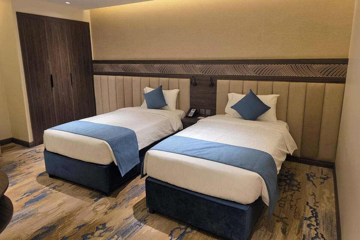 Habitación de hotel con dos camas, un armario de madera, alfombra estampada y un teléfono instalado en la pared.