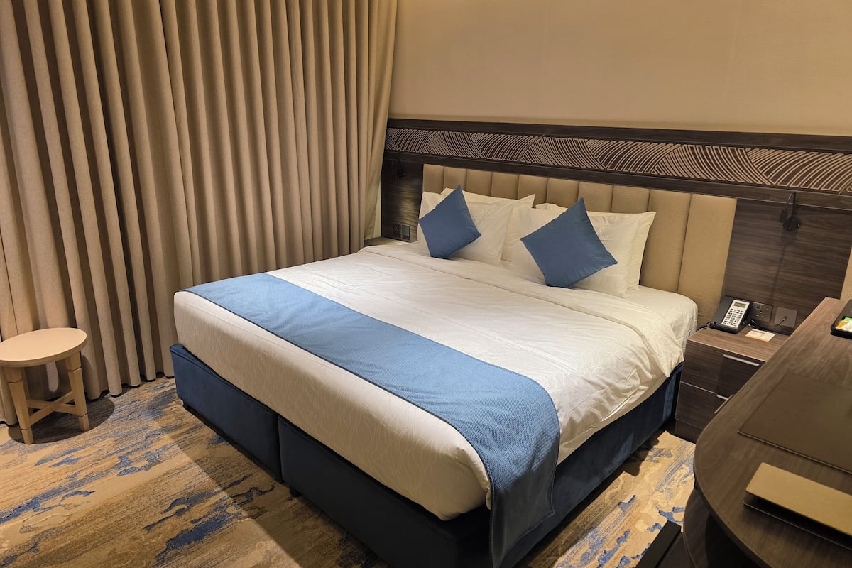 Habitación de hotel con una cama grande, una mesita de noche, una silla y un escritorio con teléfono.