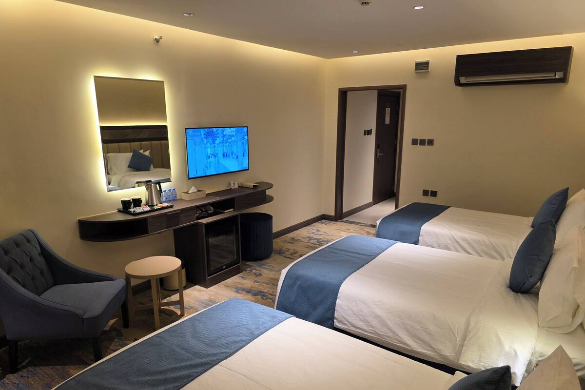 Habitación de hotel con dos camas, un escritorio, un televisor de pantalla plana, una silla y un taburete pequeño.
