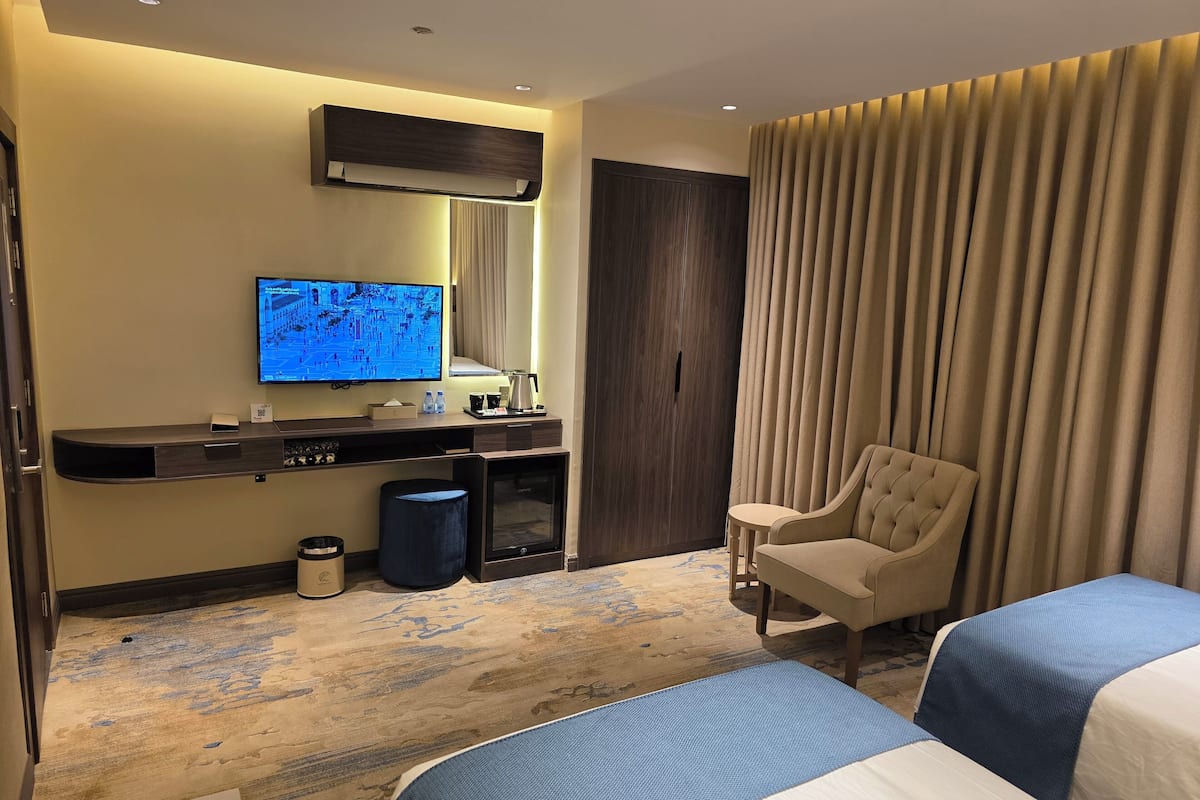 Habitación de hotel con televisor, escritorio, una silla y dos camas.