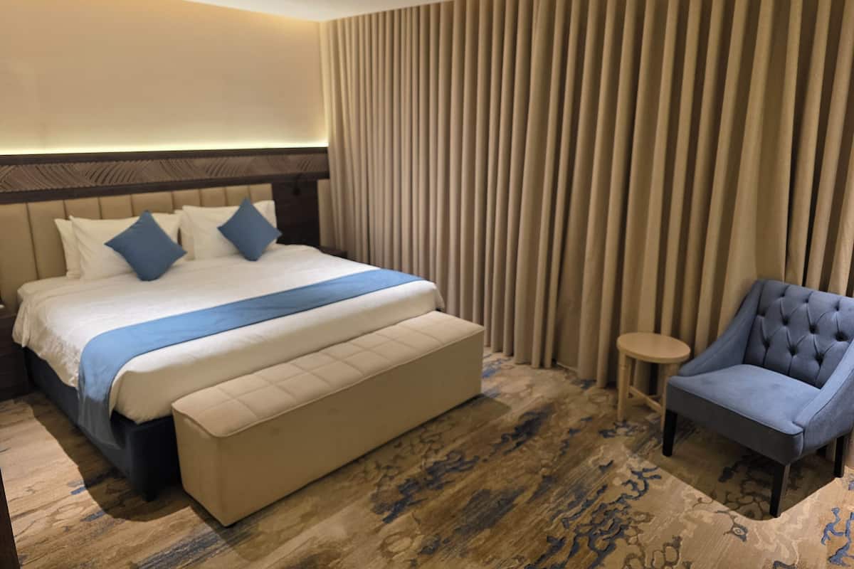Una habitación de hotel con una cama grande, una mesita redonda y un sillón azul.