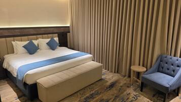 A hotel room with a large bed, a small round table, and a blue armchair.