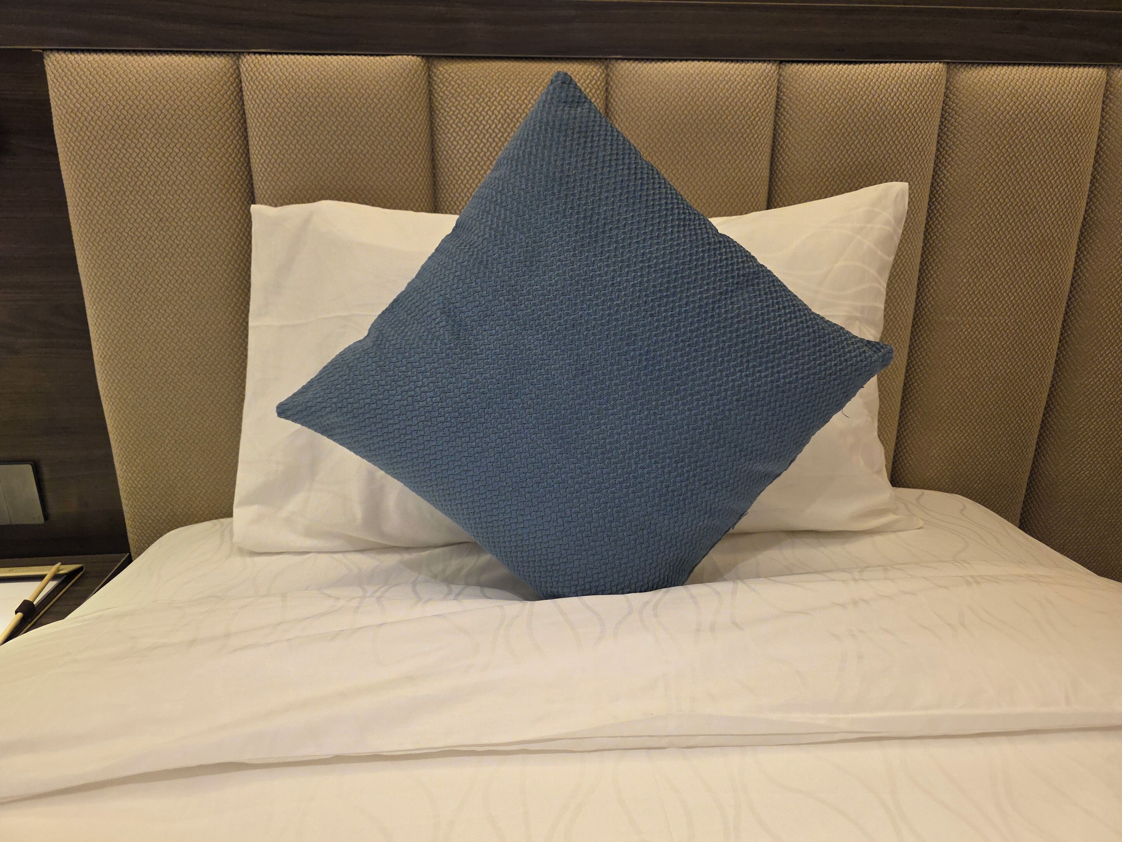 A bed with a headboard, white bedding, and a blue pillow.
