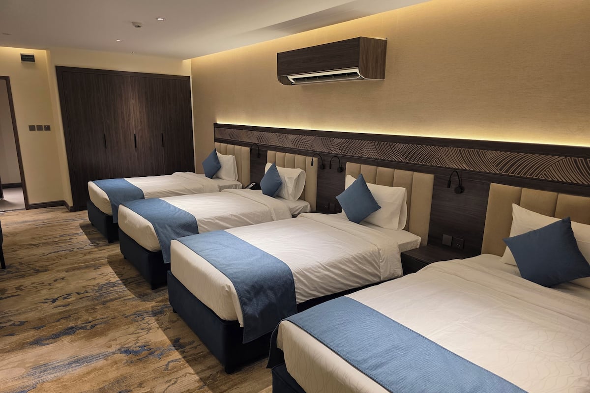 Habitación de hotel con tres camas, un armario grande de madera oscura y un equipo de aire acondicionado en la pared.