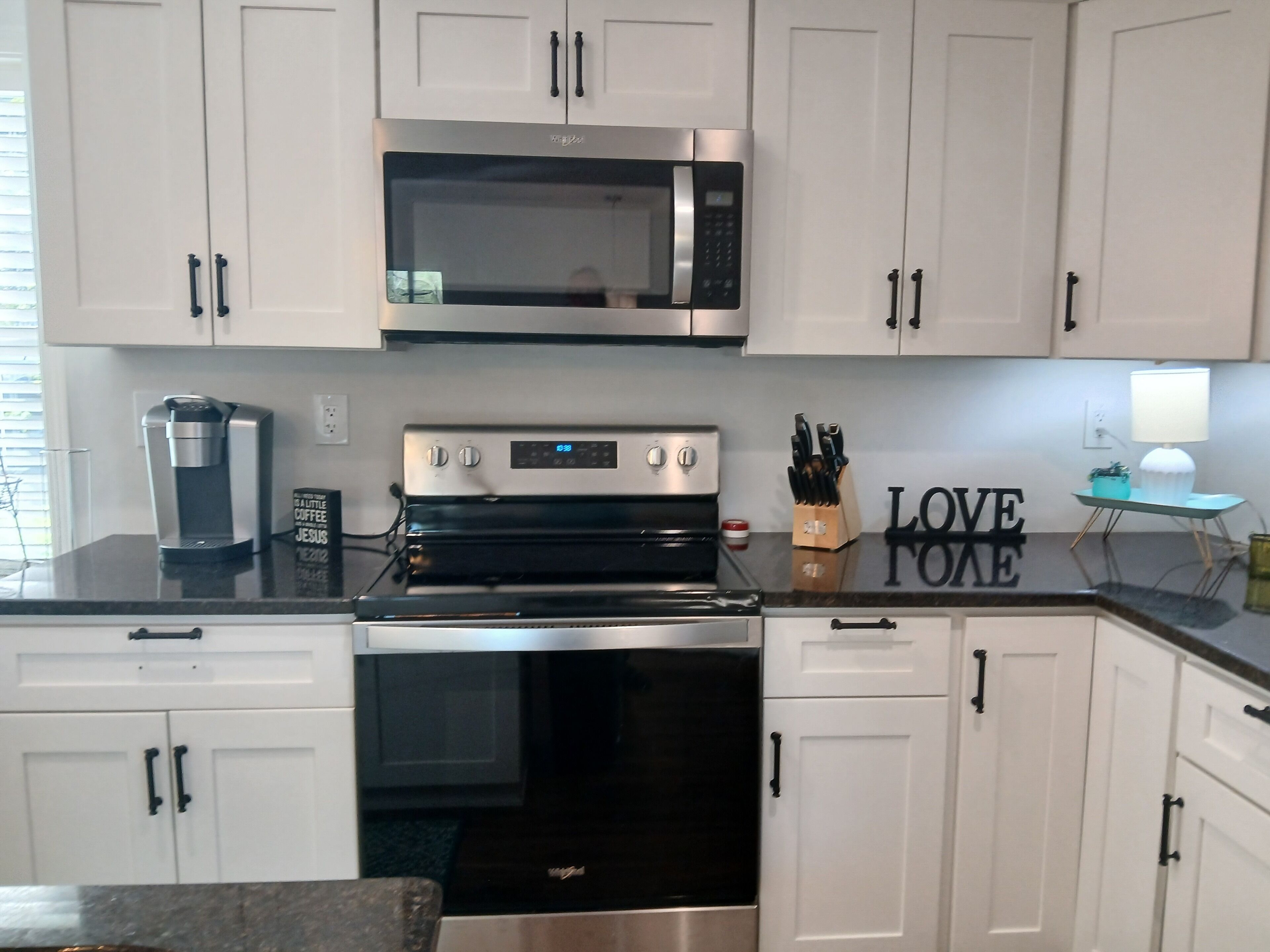 A kitchen with white cabinets, a stainless steel microwave, a coffee maker, and a stove.