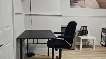 A small, modern room with a wooden floor, a black office chair, a white table, and a coffee maker.