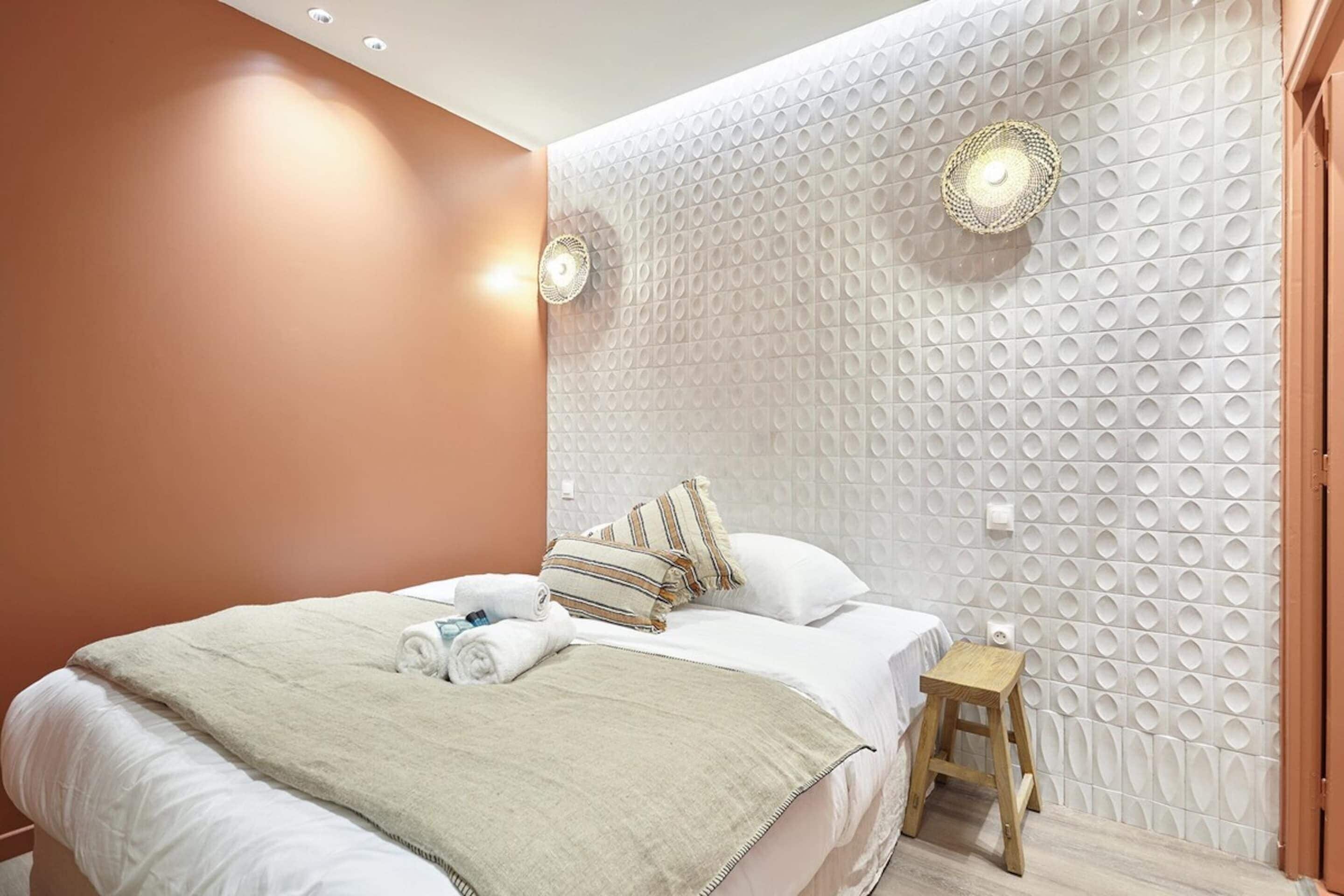 A modern hotel room with a large bed, a small stool, and a textured wall.
