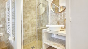 A modern bathroom with a glass-enclosed shower, a white sink, and a round mirror. - Charming Apartment With AC - Le Marais-beaubourg (Paris)
