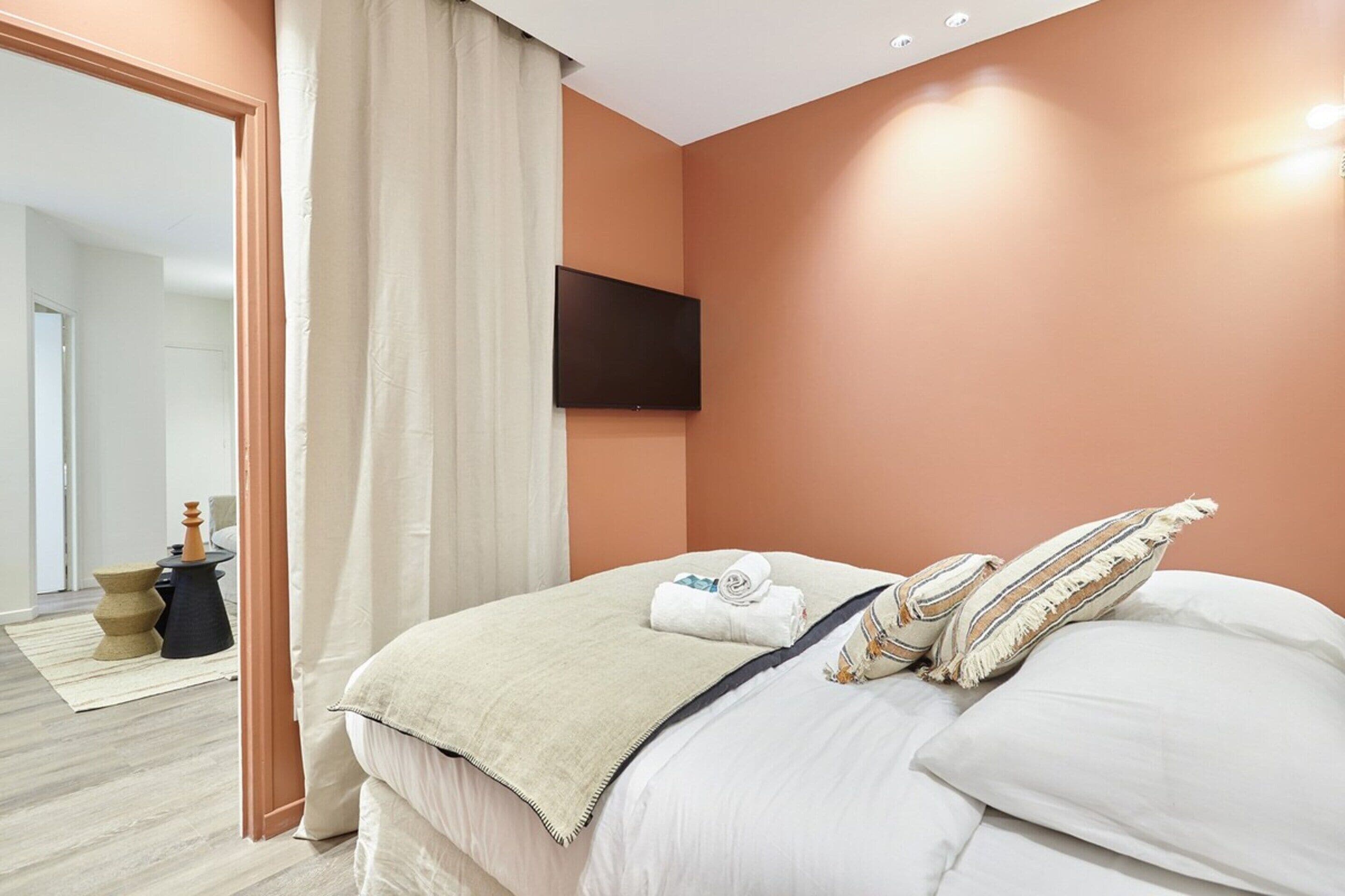 Een hotelkamer met een bed, een flatscreen televisie aan de muur en uitzicht op de gang.