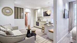 A modern living room with a sofa, a coffee table, and a TV. There is a kitchen area with a dining table and chairs. - Charming Apartment With AC - Le Marais-beaubourg (Paris)