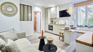 A modern kitchen with white cabinets, a built-in oven, and a dining area with a small island. - Charming Apartment With AC - Le Marais-beaubourg (Paris)