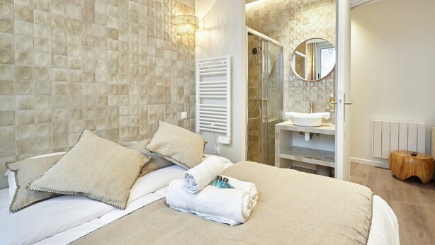 A modern hotel room with a large bed, a bathroom with a glass shower, and a round mirror. - Charming Apartment With AC - Le Marais-beaubourg (Paris)