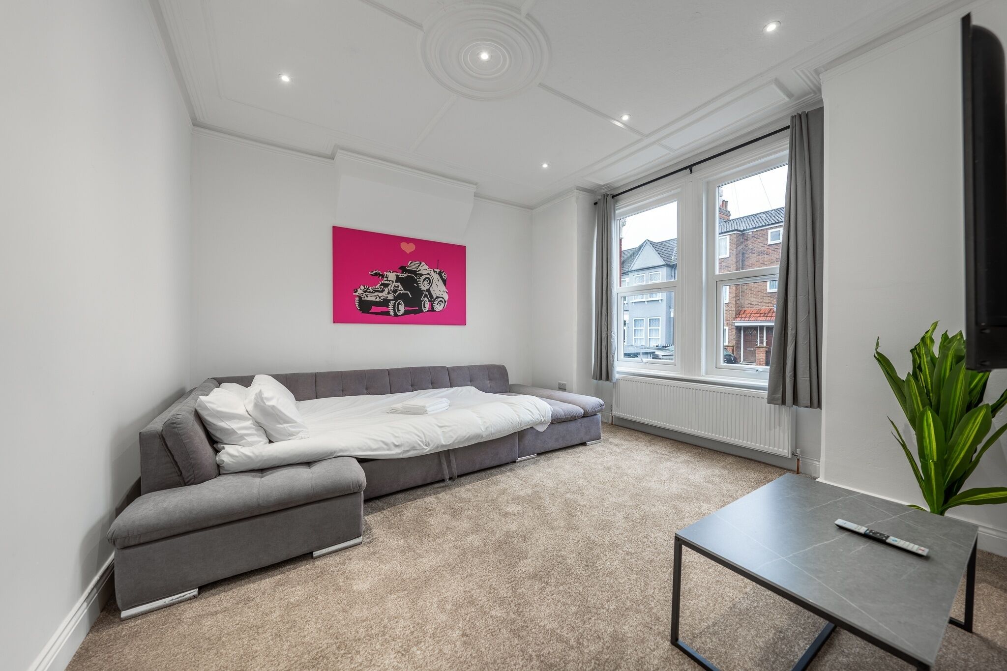 A modern living room with a grey sofa, a small table, and a large window with a view of buildings.