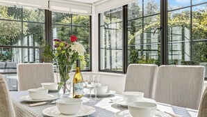 Un comedor con una mesa dispuesta para cuatro personas, ventanas amplias y un jarrón con flores.