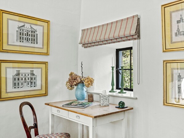 Una habitación con escritorio, cuadros, ventana con vistas y una silla.