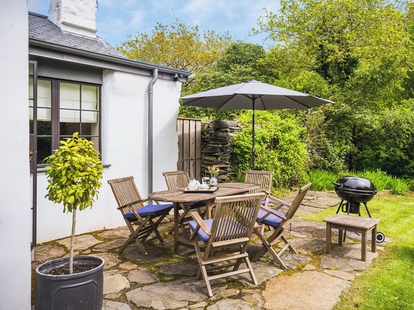An outdoor patio with a stone table and chairs, a barbecue grill, and a potted plant.