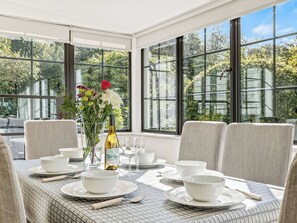 A dining area with a table set for four, large windows, and a vase with flowers.