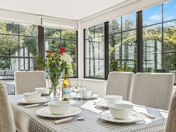 Ein Essbereich mit einem Tisch für vier Personen, großen Fenstern und einer Vase mit Blumen.