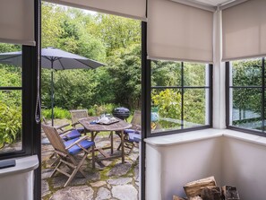 Una habitación con vista a un jardín, una mesa con sillas y una parrilla.