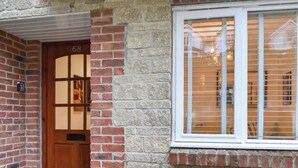 A brick house with a wooden door marked "68" and a window with blinds.