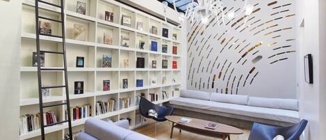 Une bibliothèque moderne avec des étagères blanches, un espace de lecture en mezzanine et un lustre.