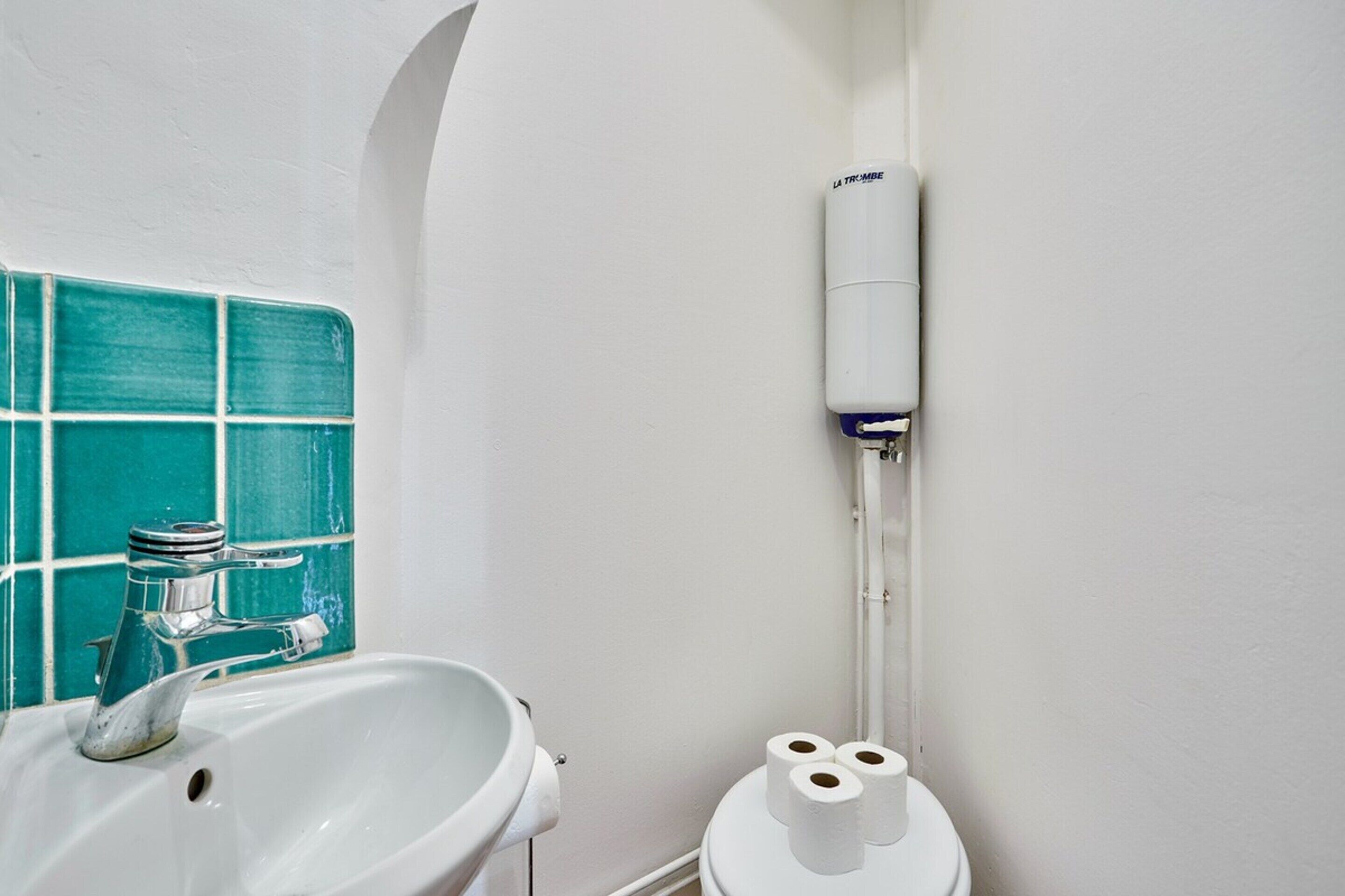A bathroom with a white sink, a turquoise tiled wall, and a toilet with two rolls of toilet paper.