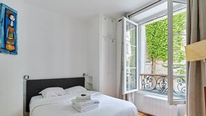 Un dormitorio con cama, ventana con vistas a zonas verdes y un cuadro en la pared.
