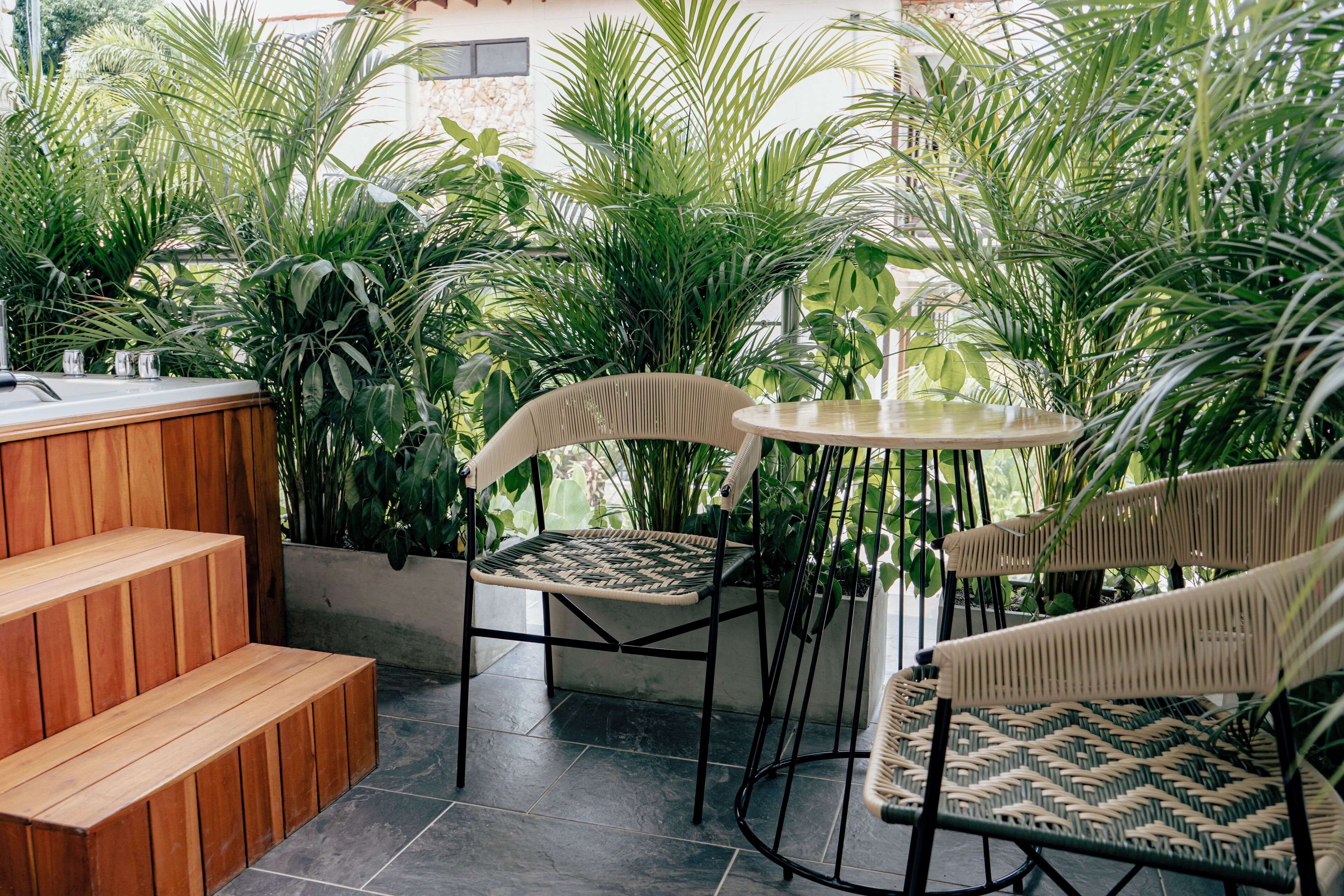 Un patio con mobiliario de madera y una mesa redonda rodeada de plantas verdes exuberantes.