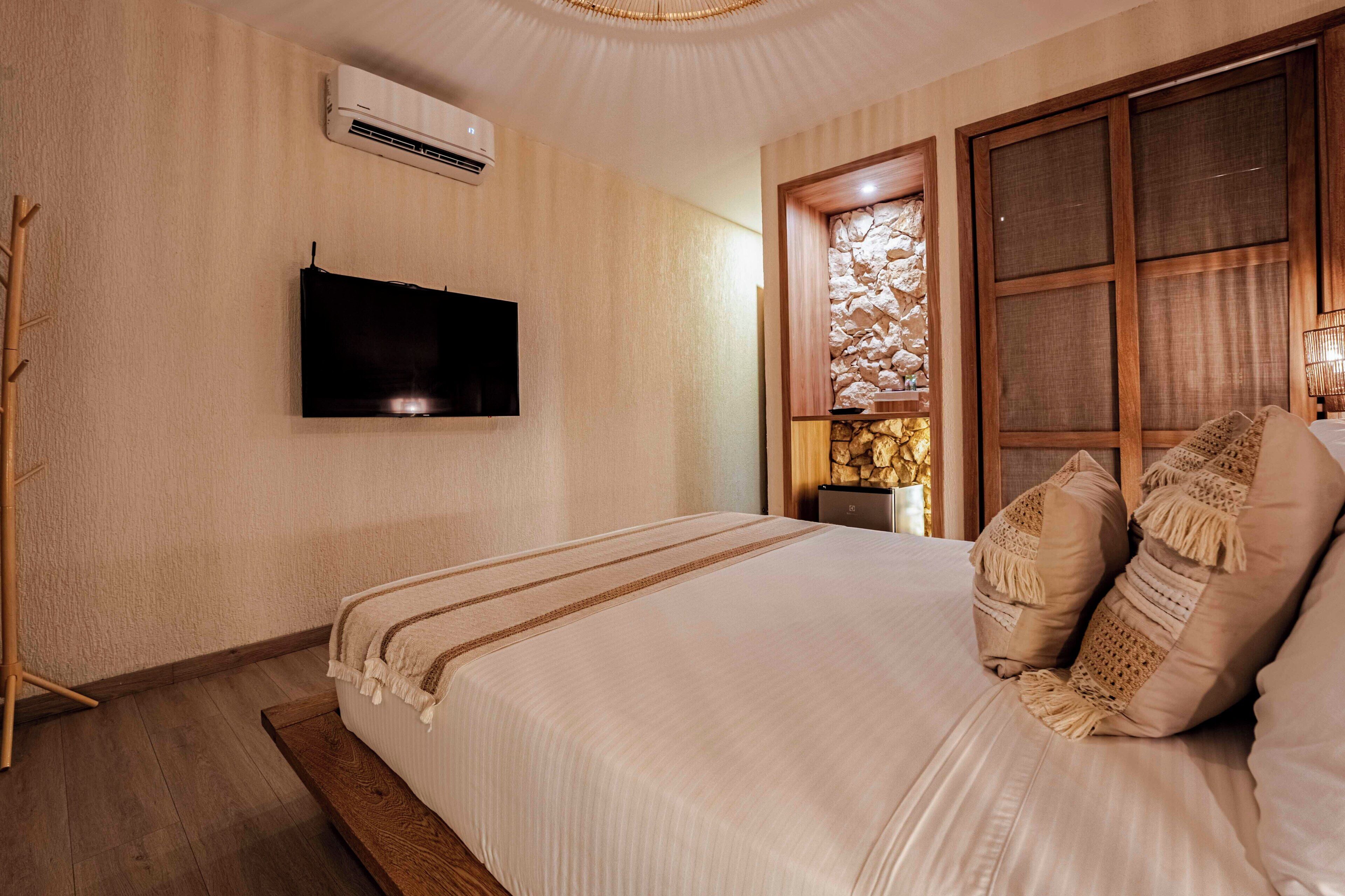 A bedroom with a bed, a mounted TV, a wall-mounted air conditioner, and a window with a stone wall.
