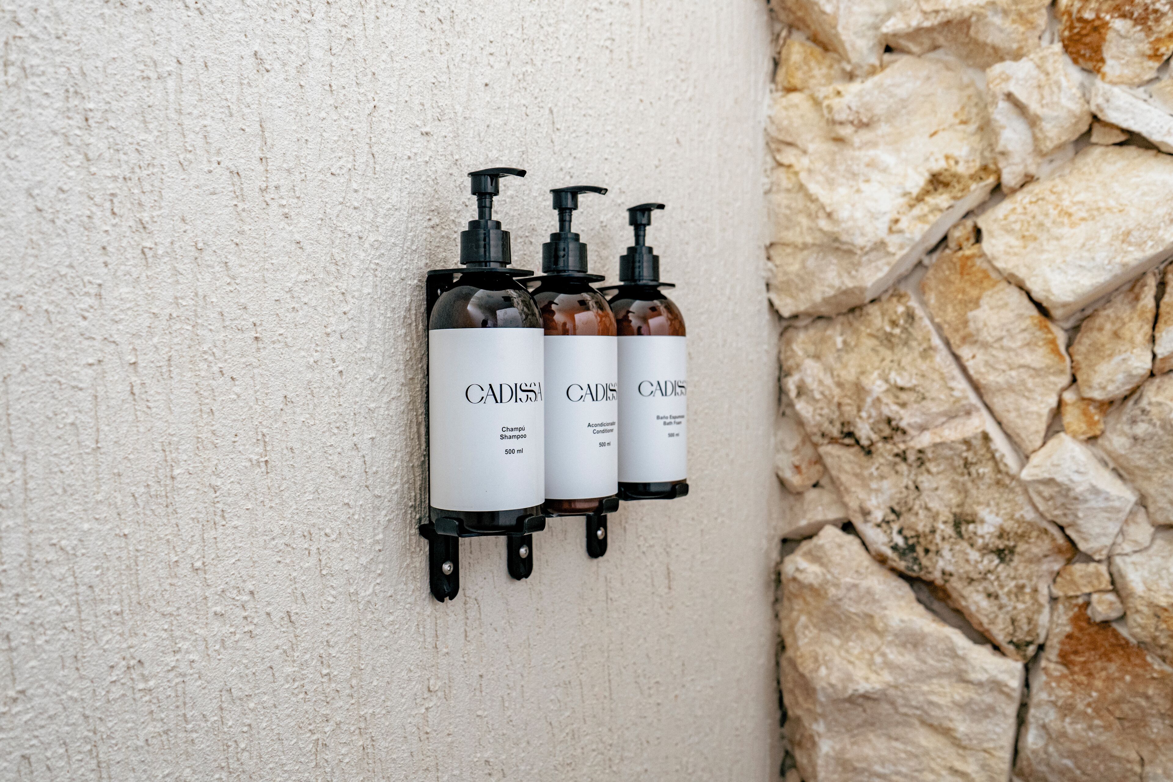 Three bottles of Cadis shampoo and conditioner mounted on a textured wall.