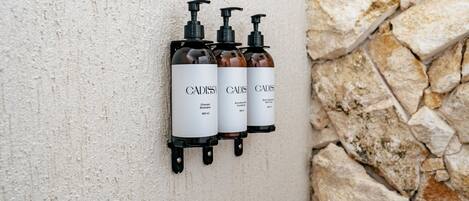Three bottles of Cadis shampoo and conditioner mounted on a textured wall.