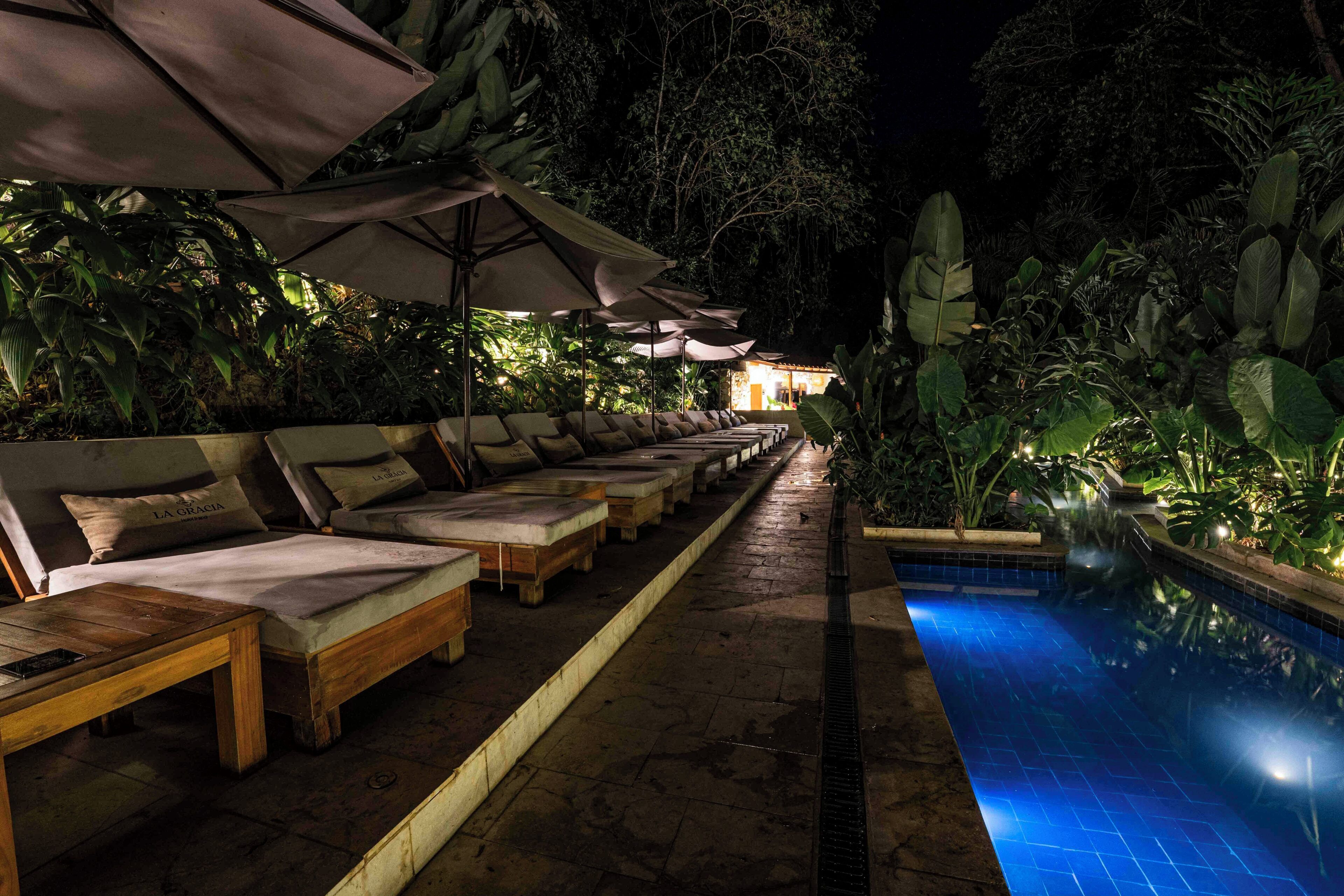 A poolside area with lounge chairs and umbrellas, surrounded by lush greenery.
