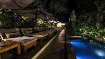 A poolside area with lounge chairs and umbrellas, surrounded by lush greenery.