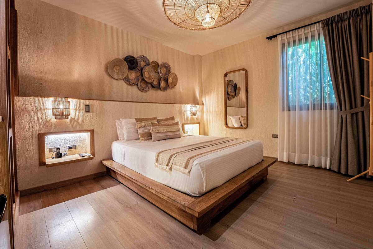 Un dormitorio con cama, lámparas de noche, una ventana con cortinas y un espejo montado en la pared.