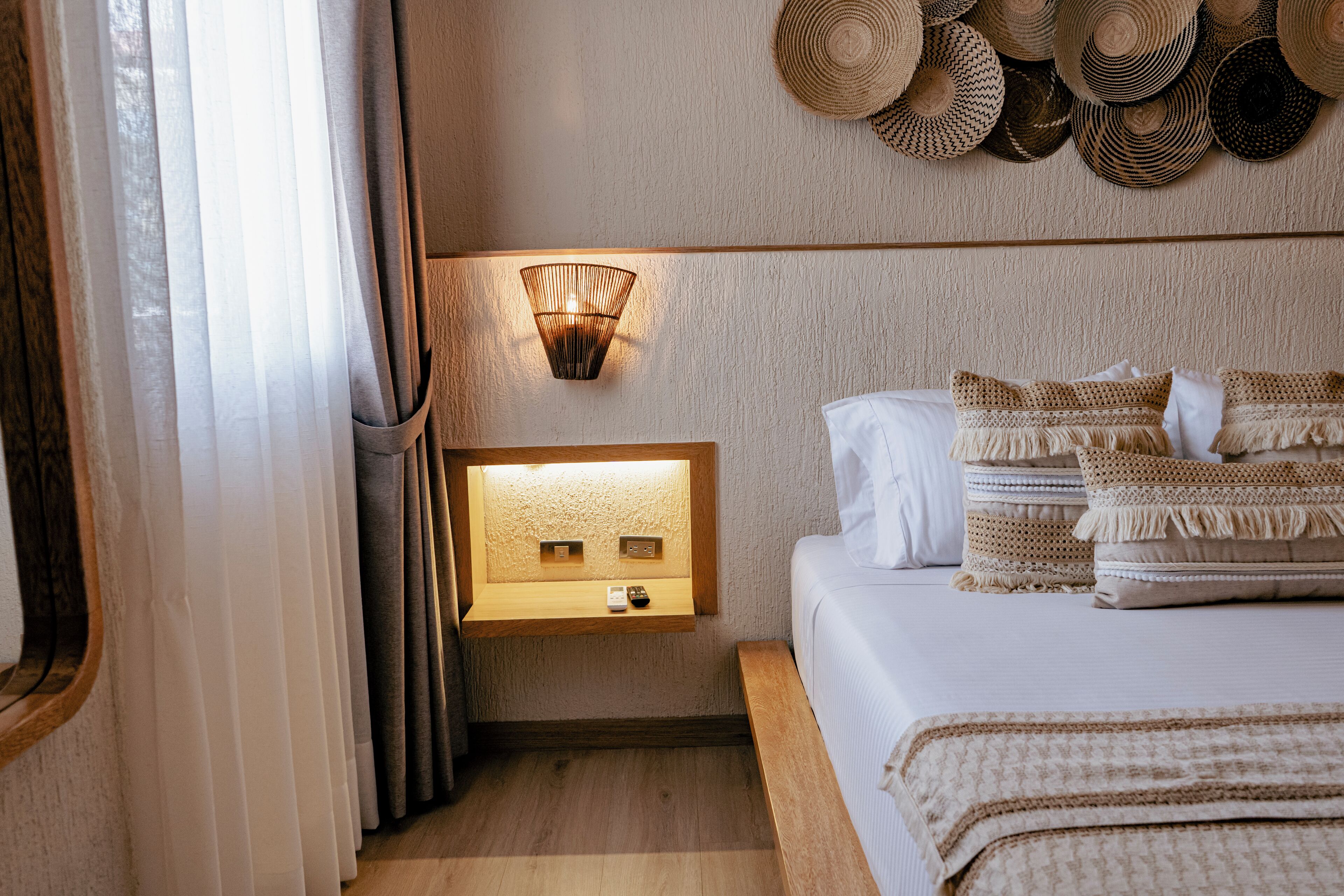 A bedroom with a bed, bedside table, wall-mounted light, and a wall with woven baskets.