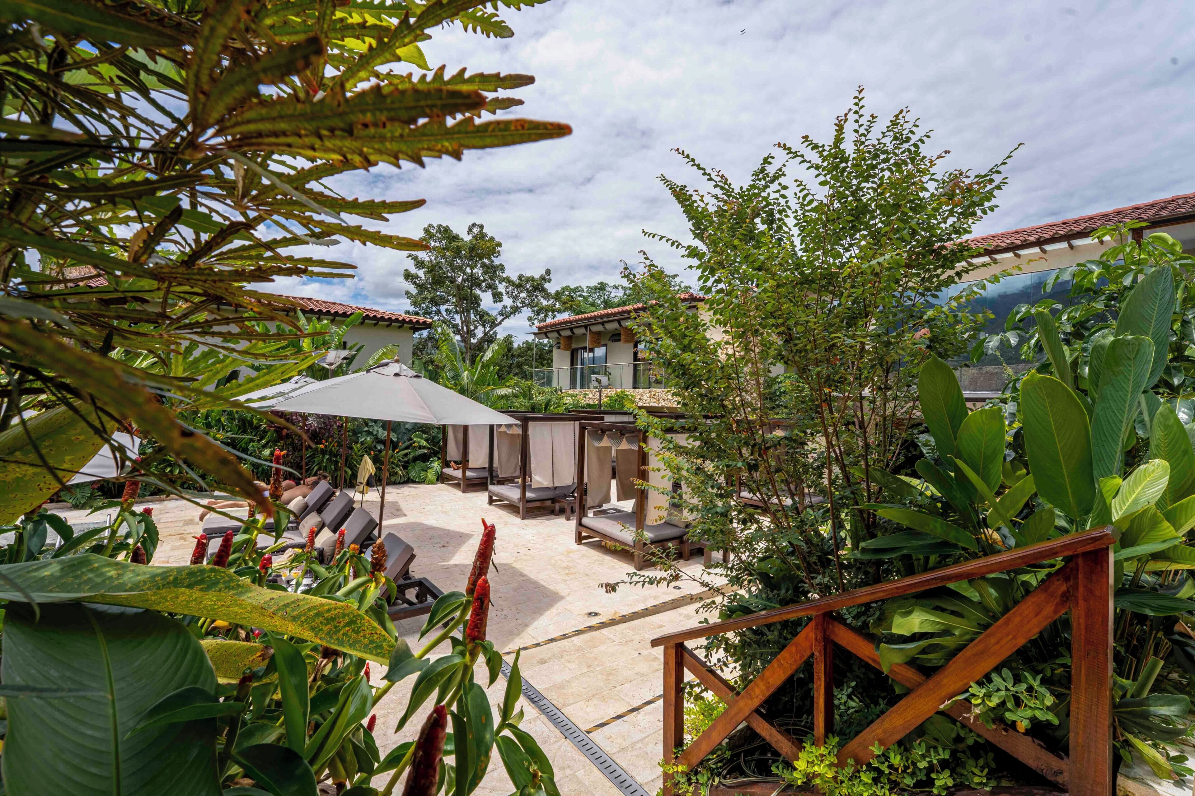 Un patio con mobiliario exterior, una escalera y abundante vegetación.