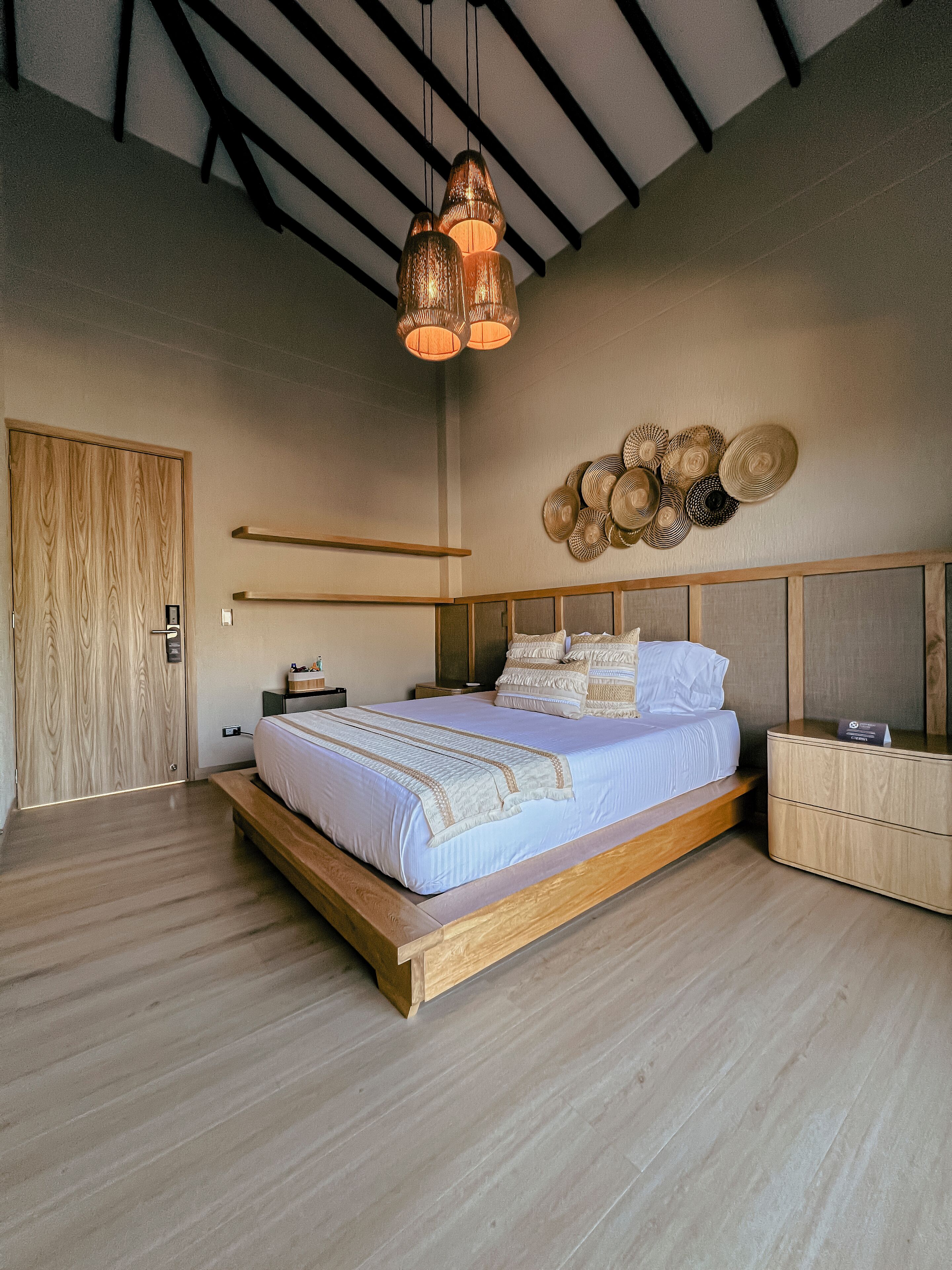 A modern bedroom with a wooden bed, bedside tables, a wall-mounted light fixture, and a decorative wall art piece.