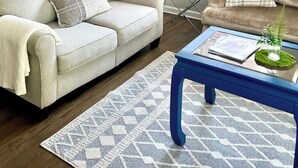 Una sala de estar con un sofá color beige, una mesa de centro azul y un tapete estampado.