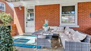 Un patio techado con una mesa y un sofá, un muro de ladrillo y una ventana.