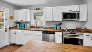 Una cocina moderna con armarios blancos, un lavavajillas de acero inoxidable, una estufa a gas y un microondas.