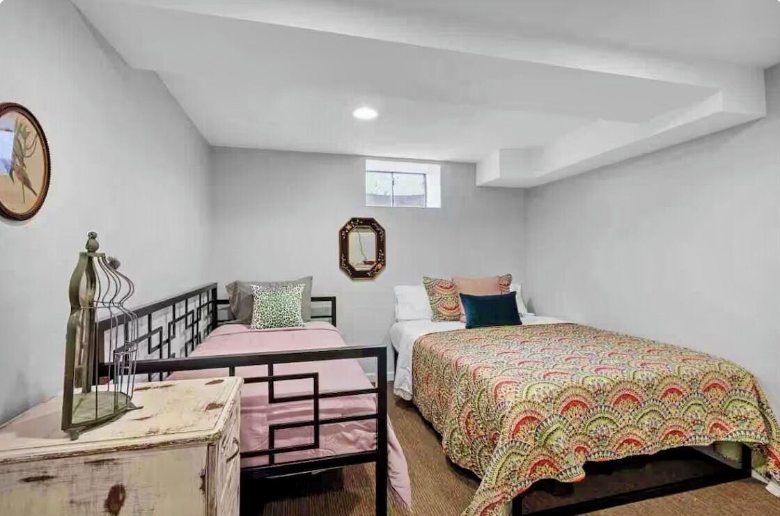 A bedroom with two beds, a small window, and a mirror on the wall.