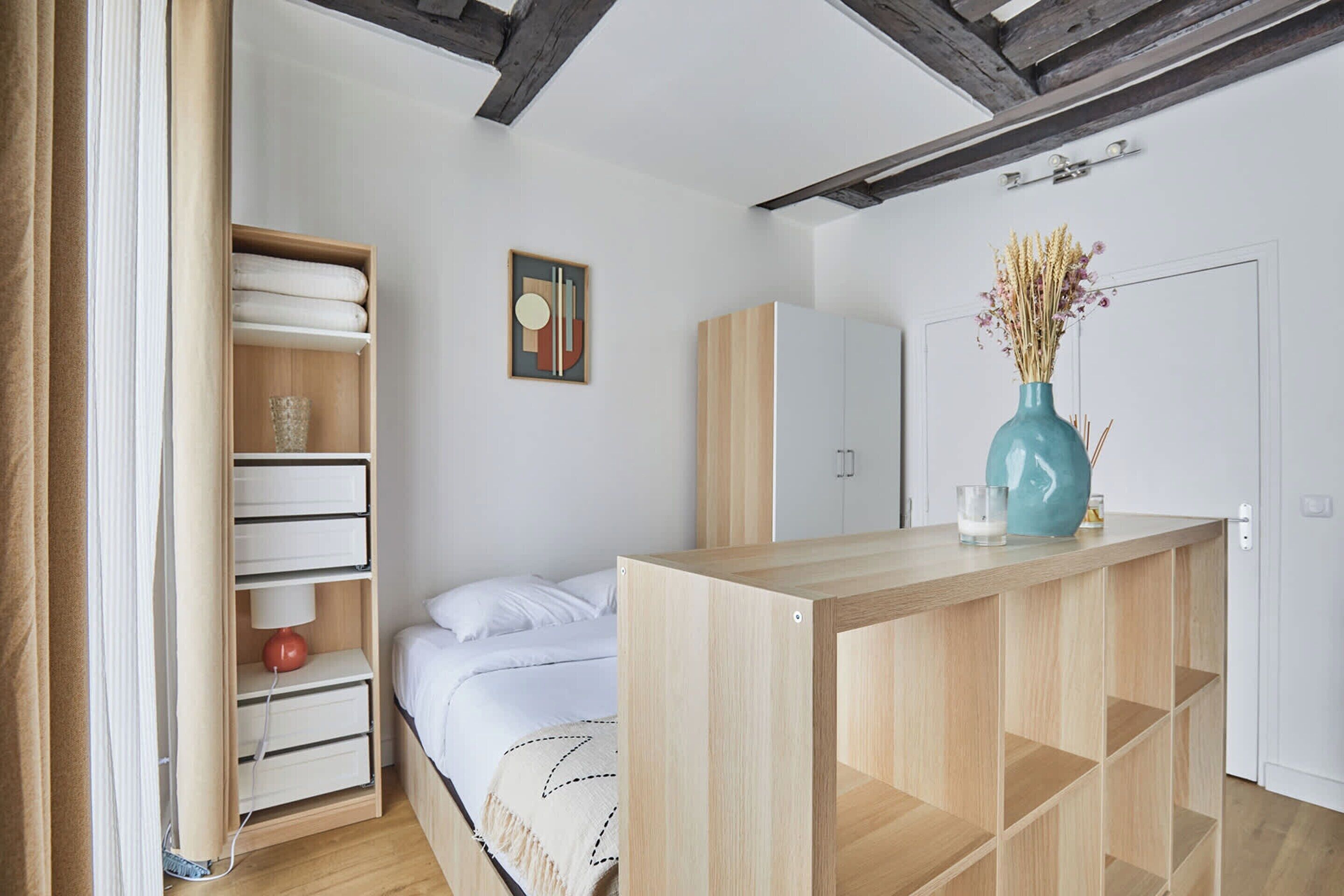 A bedroom with a bed, a wooden nightstand, a wardrobe, and a shelf with towels.