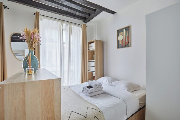 A bedroom with a bed, a bedside table with a vase, a mirror, and a painting on the wall.
