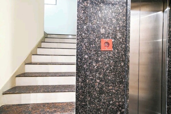Una escalera con un muro de granito y un botón de emergencia rojo.