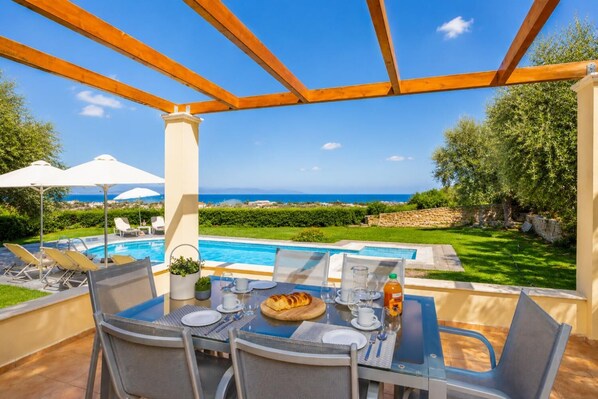 Ein Essbereich im Freien mit Blick auf einen Pool, ein Tisch für zwei Personen und eine Pergola darüber.