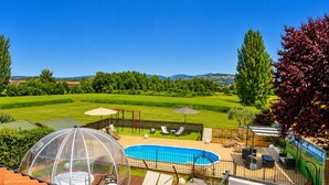 Un jardin avec une piscine, des chaises longues, un barbecue et une vue sur la campagne.