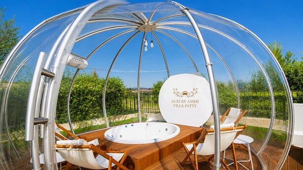 Une structure en forme de dôme transparent abritant un jacuzzi, une terrasse en bois et un espace salon extérieur.